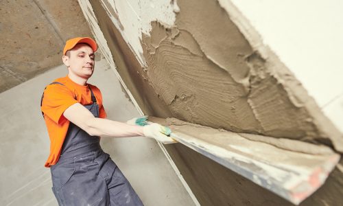 Plasterer spraying thin-layer putty plaster finishing on brick wall