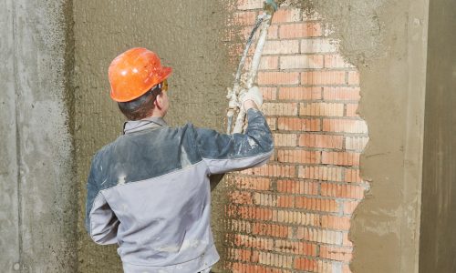 Plasterer operating sprayer equipment machine for spraying thin-layer putty plaster finishing on brick wall